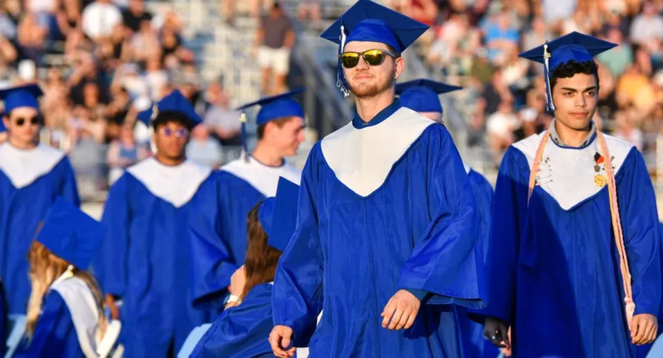 Un gruppo di diplomati in toga blu del Daniel McIntyre Collegiate Institute cammina insieme durante una cerimonia di diploma.