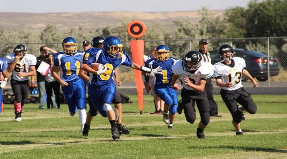 Un gruppo di giocatori di calcio si allena sul campo sportivo della Huntington High School davanti a un paesaggio collinare.