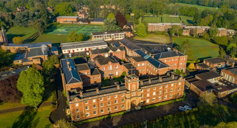 Il grande edificio in mattoni con torre centrale e giardini nel campus della King Edward's Witley School è circondato da alberi.