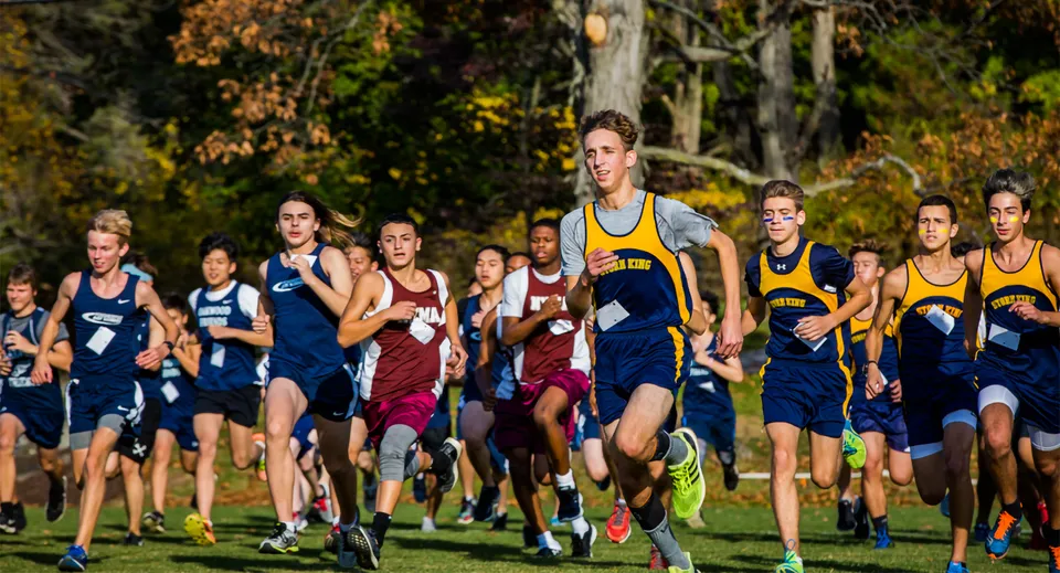 Studenti della The Storm King School corrono durante una gara di cross-country in un bosco autunnale.