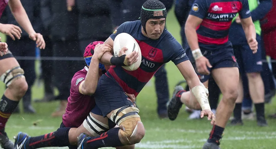 Un giocatore di rugby della Portmarnock Community School corre con la palla in campo mentre viene placcato.
