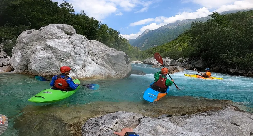 Gli studenti del Coláiste Naomh Cormac pagaiano in canoe colorate su un fiume circondato dal verde e da scogliere rocciose.