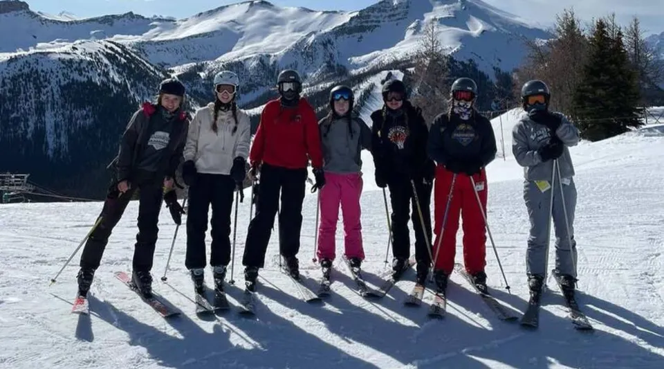 Un gruppo di studenti della Bawlf School si trova in inverno su un pendio innevato con le montagne sullo sfondo.
