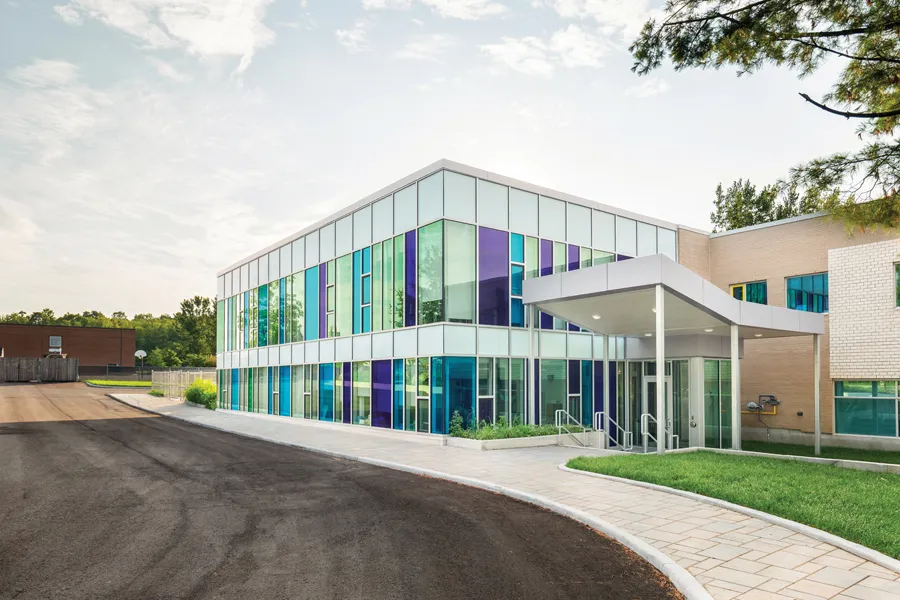El edificio escolar de varias plantas de la École secondaire publique Carrefour Jeunesse con fachada de cristal y paneles de colores se encuentra en un entorno verde.