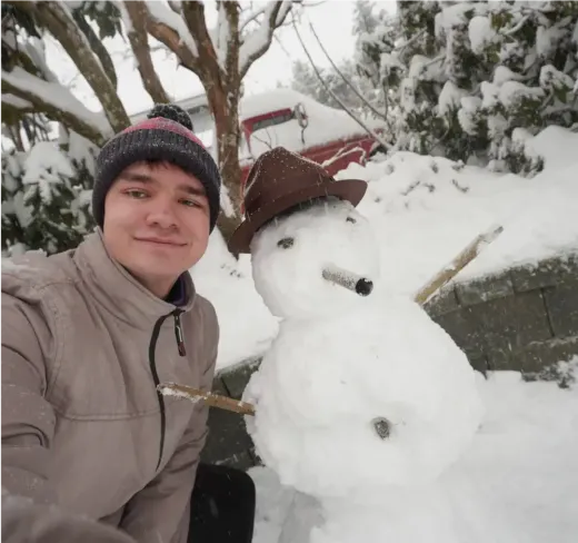 Stefan lächelt neben einem Schneemann in einer Winterlandschaft in Kanada