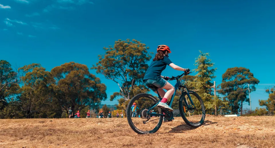 Una persona in abbigliamento sportivo va in bicicletta su un sentiero circondato da alberi all'interno del campus della Benowa State High School.