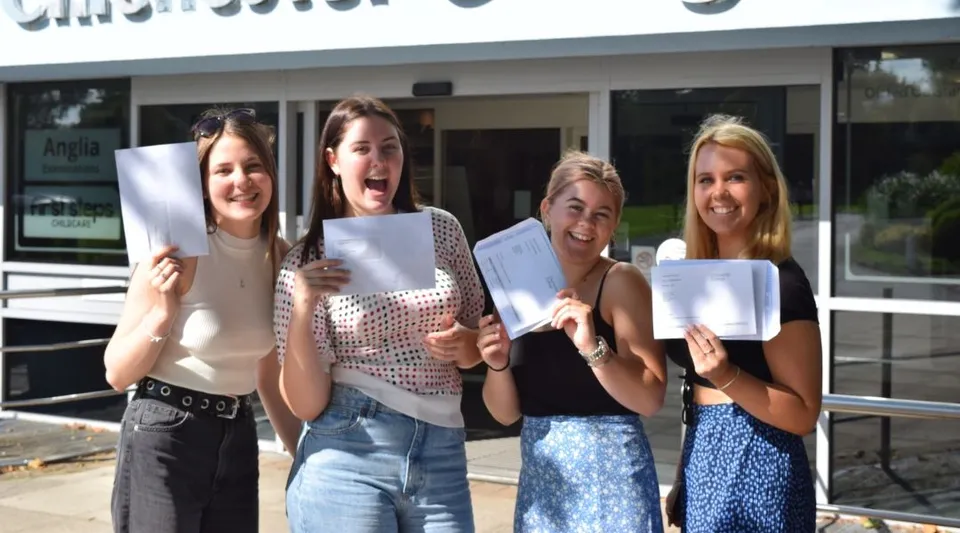 Quattro studentesse tengono in alto dei documenti davanti a un edificio del Chichester College.