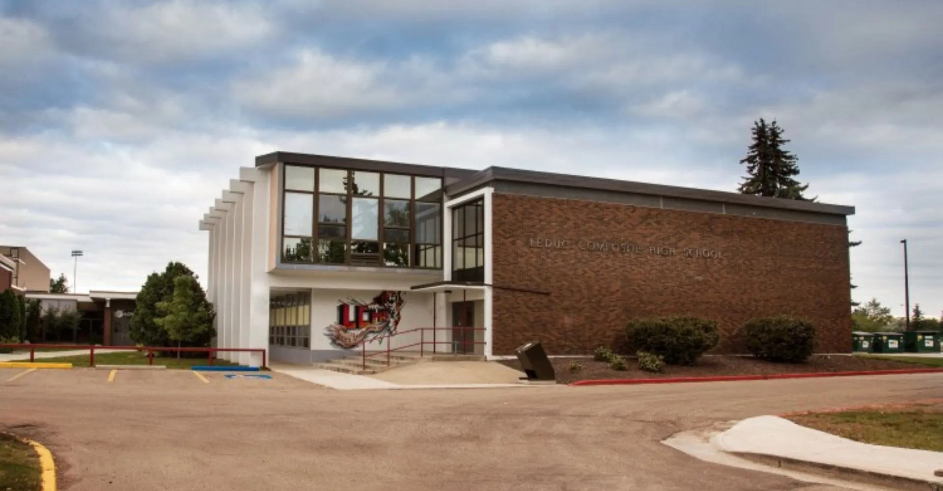 Il moderno edificio a più piani in mattoni della Leduc Composite High School, con ampie finestre e una caratteristica porta d'ingresso, è circondato da alberi.