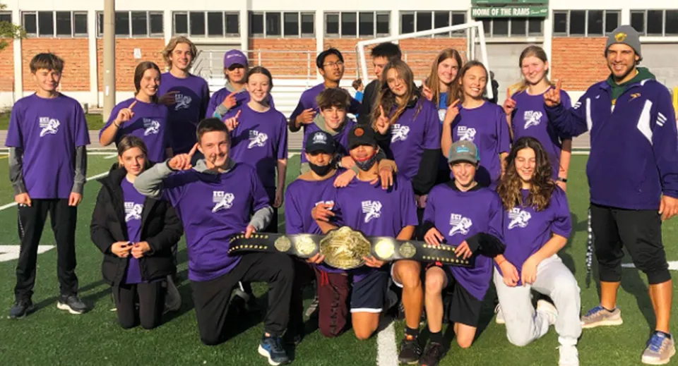 Un gruppo di studenti con magliette viola si trova insieme sul campo sportivo dell'Etobicoke Collegiate Institute davanti a un edificio in mattoni.