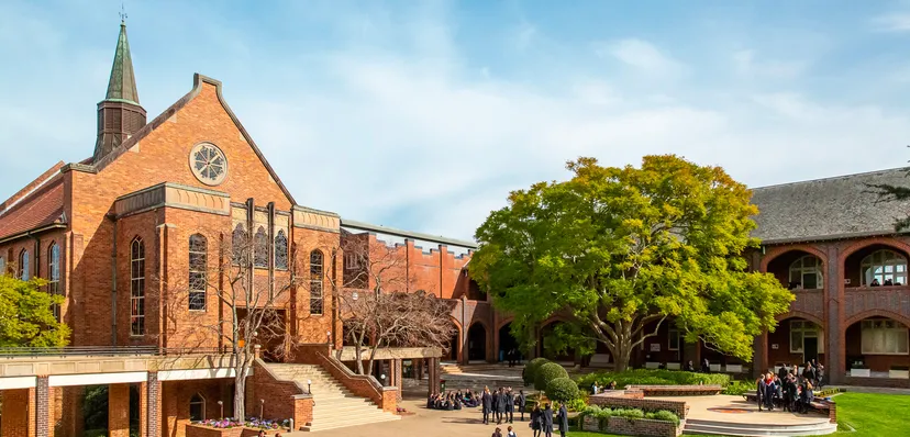L'edificio in mattoni con un'alta torre nel campus del Pymble Ladies College è circondato da una verde vegetazione e da un vialetto pavimentato.
