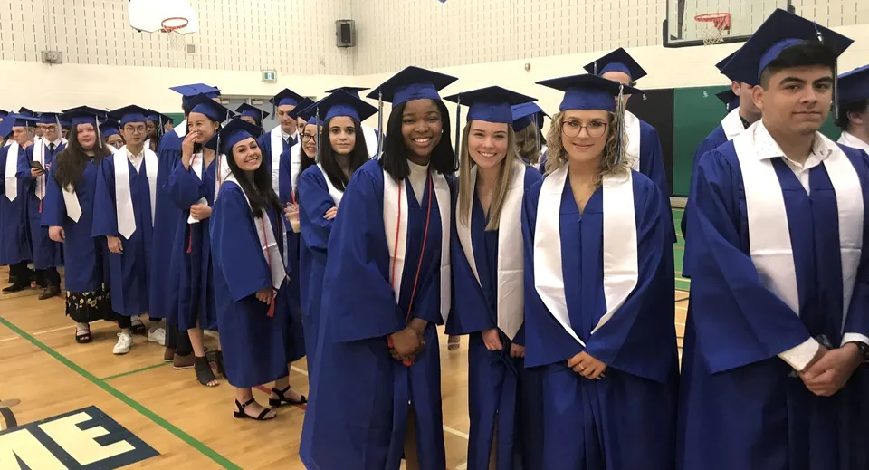 Un gruppo di diplomati in toga blu si trova nell'aula magna della Holy Trinity Catholic High School.
