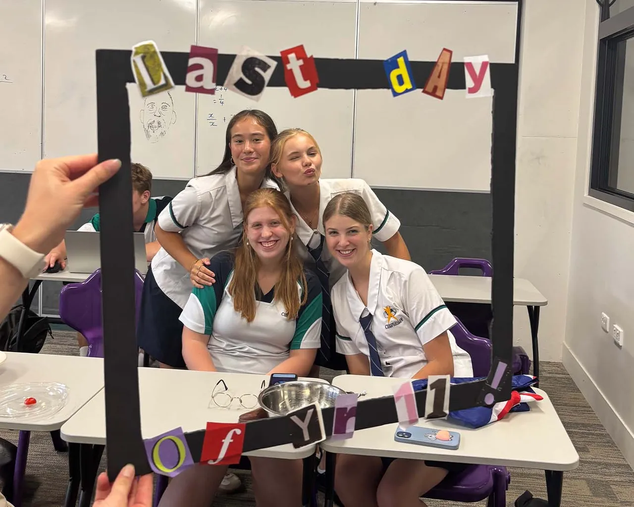 Cuatro alumnas posan en clase con un marco de cartón decorado con las palabras Last day of Yr 11