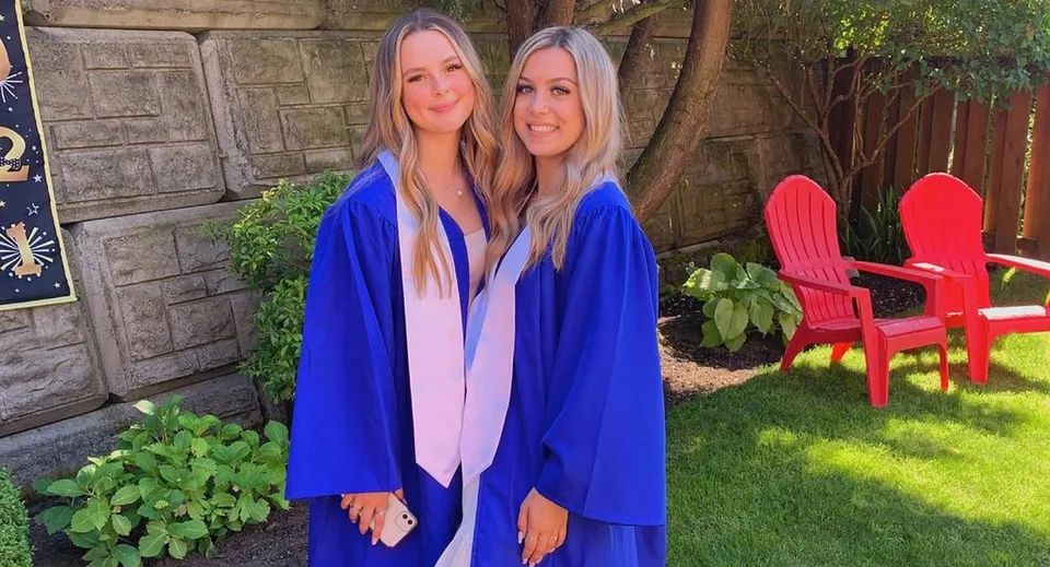 Due studentesse con lunghi capelli biondi sono insieme nel giardino della Belmont Secondary School davanti a una rigogliosa vegetazione e a una sedia Adirondack rossa.