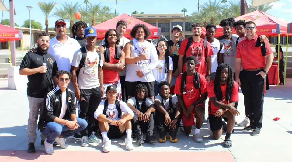 Un gruppo di studenti con adulti si trova all'aperto davanti a delle palme nel campus del College of the Desert.