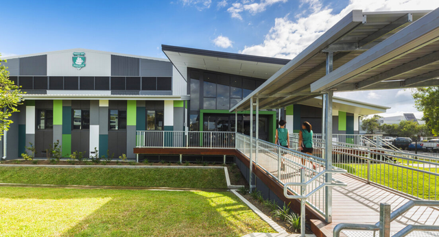 Das moderne mehrstöckige Gebäude der Trinity Bay State High School ist von einer Wiese und einem Weg mit Geländern umgeben.