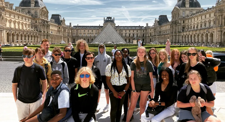Un gruppo di studenti della New Hall School in posa davanti al Museo del Louvre a Parigi con la piramide di vetro sullo sfondo.