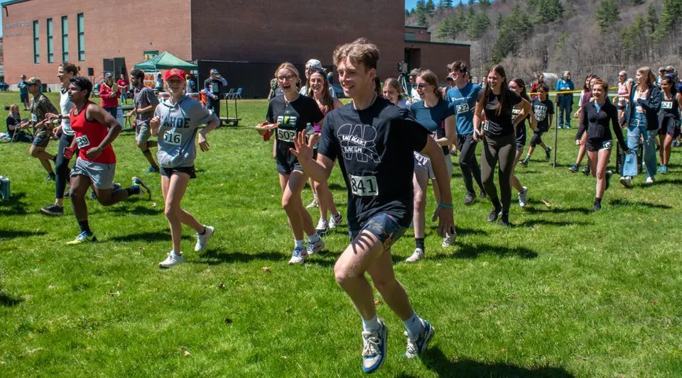 Un gruppo di studenti si riunisce su un campo sportivo davanti a un edificio in mattoni del Montpelier Roxbury Public School District.