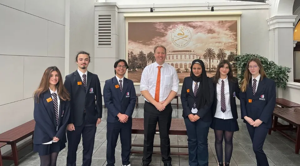 Un gruppo di studenti in uniforme scolastica si trova davanti a un grande dipinto con una vista della città all'interno della Balcatta Senior High School.