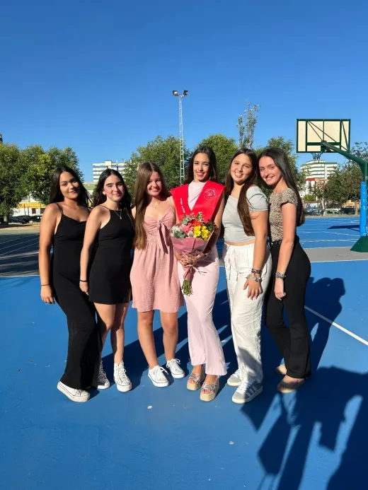Sei ragazze in posa su un campo da basket, una con un mazzo di fiori e la fascia da diploma