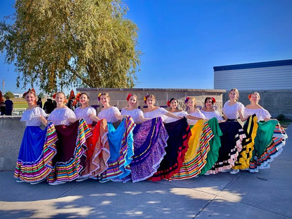 Un gruppo di donne in abiti tradizionali colorati si trova davanti a un edificio della Tri-Cities Prep Catholic High School con un pascolo sullo sfondo.