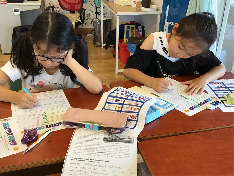Zwei Schülerinnen der Ascot International School sitzen an einem Tisch im Klassenzimmer und schreiben in Arbeitsblätter.
