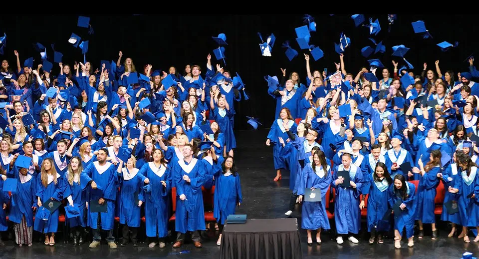 Un gruppo di studenti della Garibaldi Secondary School indossa toge da diploma blu durante una cerimonia di diploma su un palco.