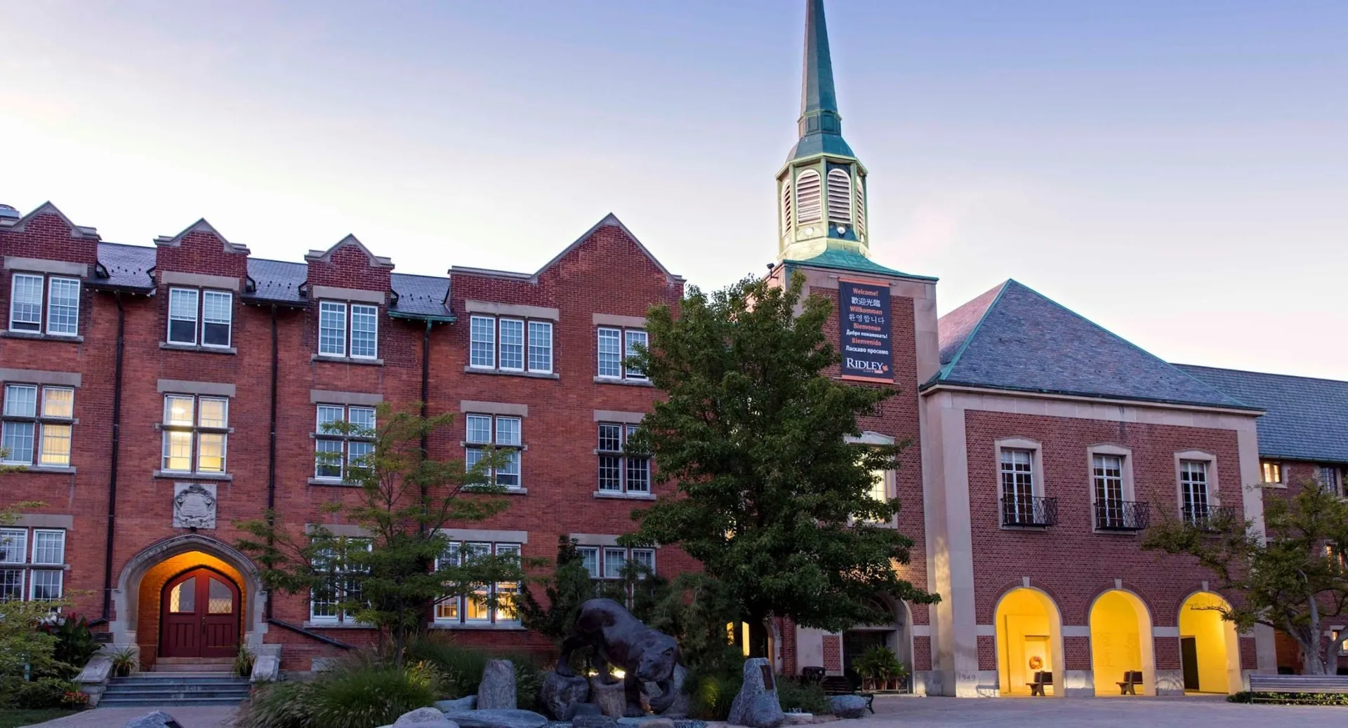 Il storico edificio in mattoni con un'alta torre nel campus del Ridley College è circondato da alberi e altri edifici.