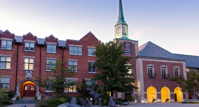 Il storico edificio in mattoni con un'alta torre nel campus del Ridley College è circondato da alberi e altri edifici.