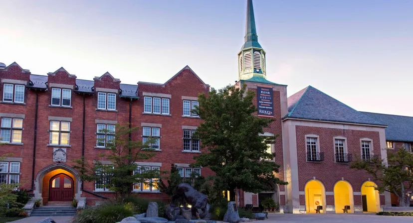 Il storico edificio in mattoni con un'alta torre nel campus del Ridley College è circondato da alberi e altri edifici.