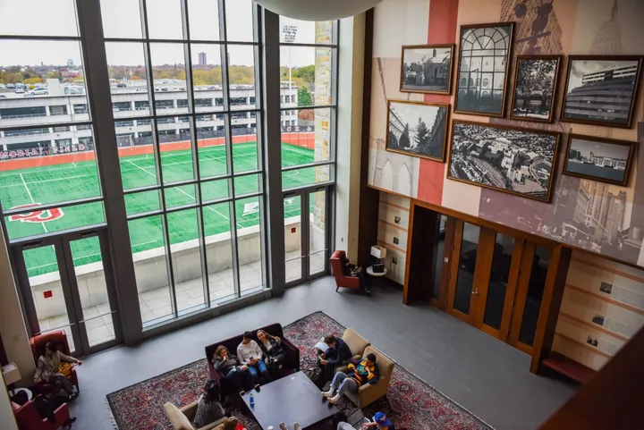 Sala comune degli studenti con divani, tappeto e vetrate affacciate sul campo sportivo del campus