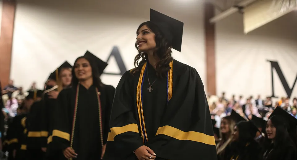 I diplomati della Xavier College Preparatory High School indossano toghe nere e si trovano in un corridoio con persone sullo sfondo.