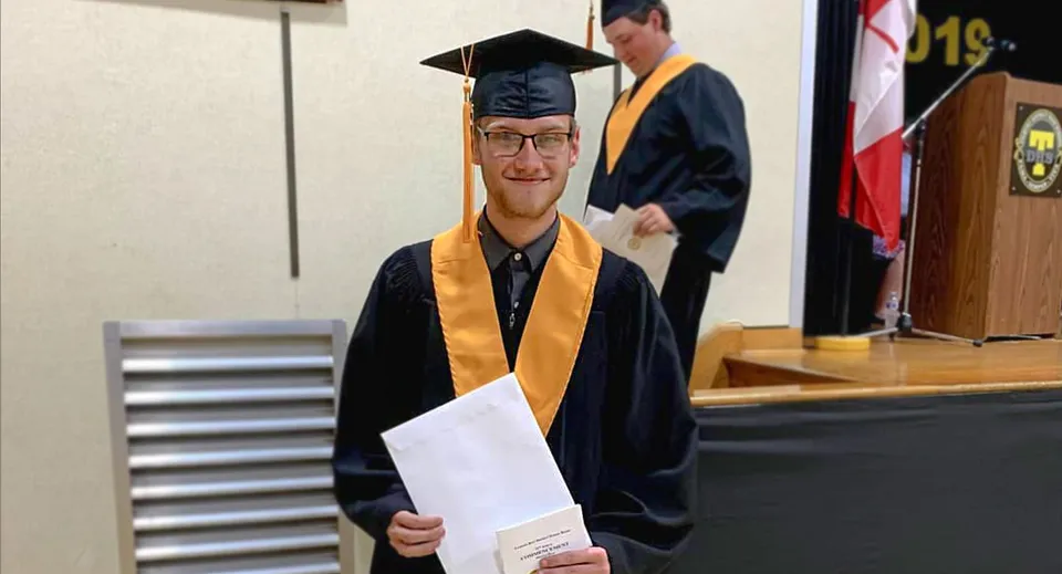 Un giovane uomo in toga da diploma con un attestato in una stanza della Tilbury District High School.