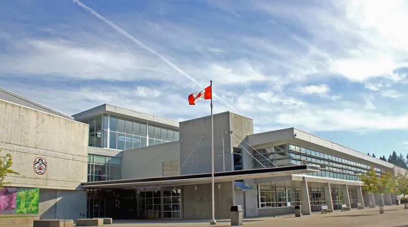 L'edificio scolastico moderno a più piani della Heritage Woods Secondary School con vetrate e la bandiera canadese sullo sfondo.