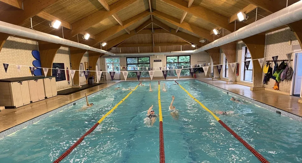 La piscina coperta con soffitto in legno e corsie tracciate all'interno del campus della Bournemouth Collegiate School con nuotatori in acqua.