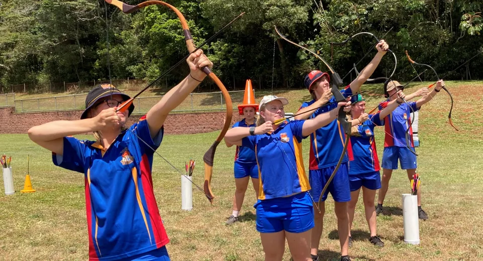 Studenti della Malanda State High School si esercitano nel tiro con l'arco all'aperto su un campo sportivo circondato dal verde.