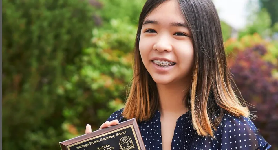 Una studentessa della Heritage Woods Secondary School sorride con foglie verdi sullo sfondo.