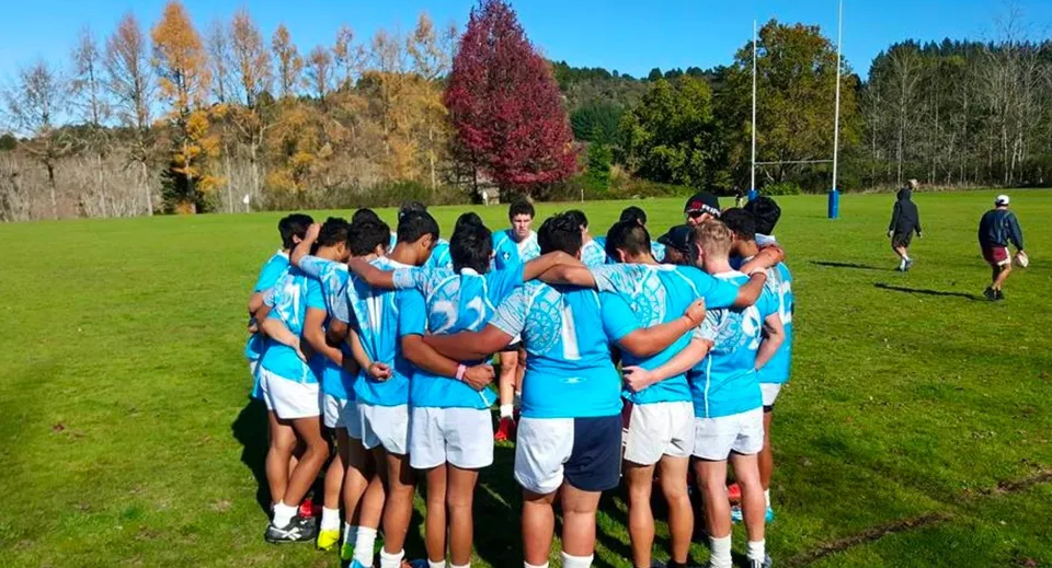 Studenti della Taumarunui High School si radunano su un prato davanti a un variopinto fogliame autunnale.