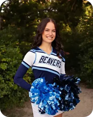 Leni sorride in divisa da cheerleader con i pompon in un giardino negli USA