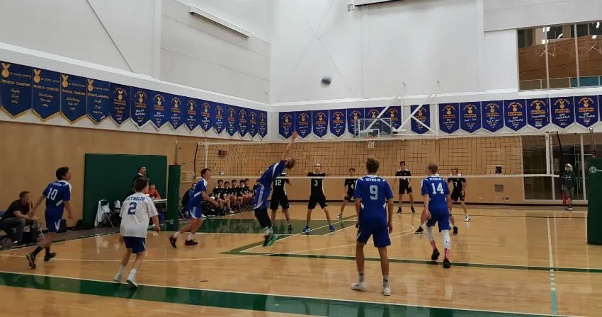 Estudiantes de la Reynolds Secondary School juegan al baloncesto en una cancha con suelo de madera y paredes blancas.