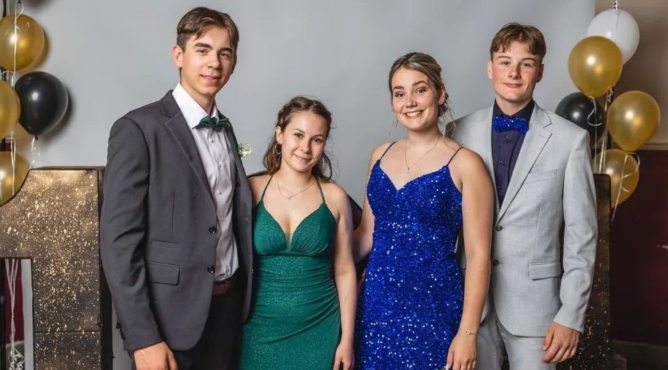 Quattro studenti del Collège de Sainte-Anne-de-la-Pocatière posano in abito da sera davanti a una parete luccicante decorata con palloncini.