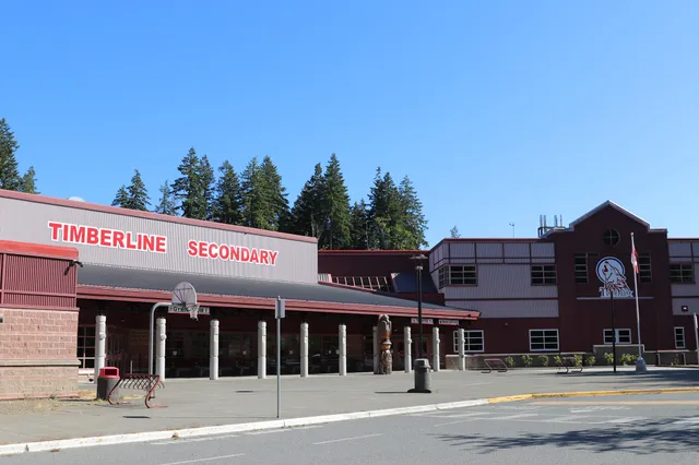 Das rote Schulgebäude der Timberline Secondary School ist von einem Wald mit hohen Kiefern umgeben.