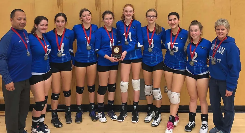 Un gruppo di giovani giocatrici di pallavolo della Chilliwack Secondary School è insieme davanti a uno sfondo di legno.