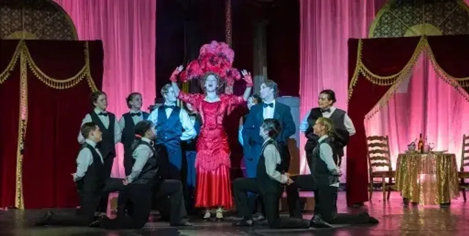 Studenti della Liberty Christian Academy stanno su un palco con tende decorative, vestiti in abiti formali e un costume rosso.