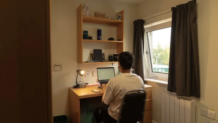 Estudiante trabajando en el escritorio de su habitación junto a la ventana