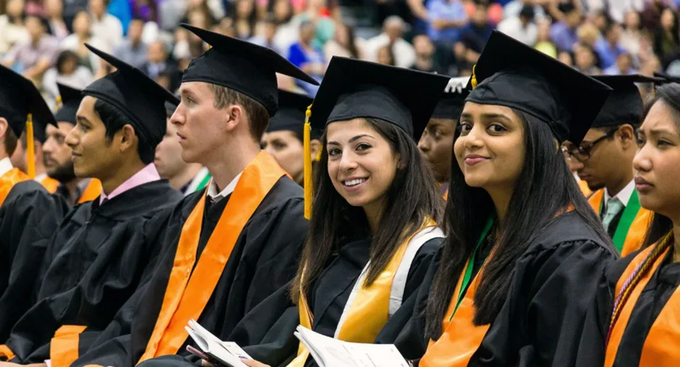 I diplomati e le diplomate della Elmwood High School sono insieme con i loro abiti da diploma e sorridono alla fotocamera.