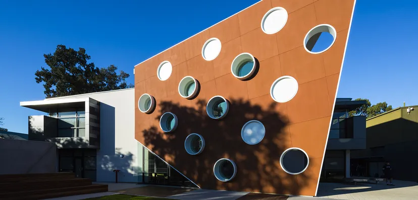 L'edificio arancione della Marryatville High School con finestre rotonde e ombre di alberi sulla facciata si staglia contro un cielo blu.