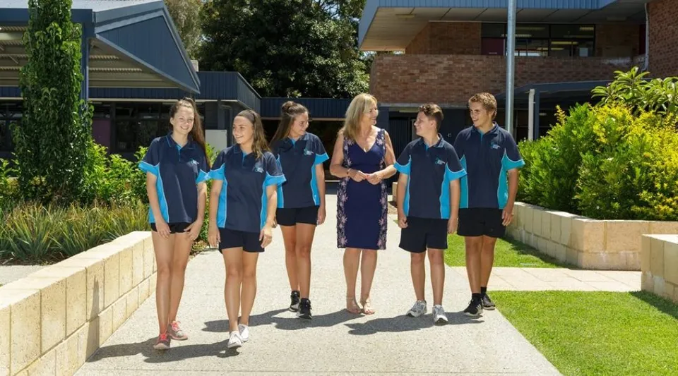 Un gruppo di studentesse in divisa blu e bianca si trova su un sentiero erboso davanti a un edificio del Southern River College.