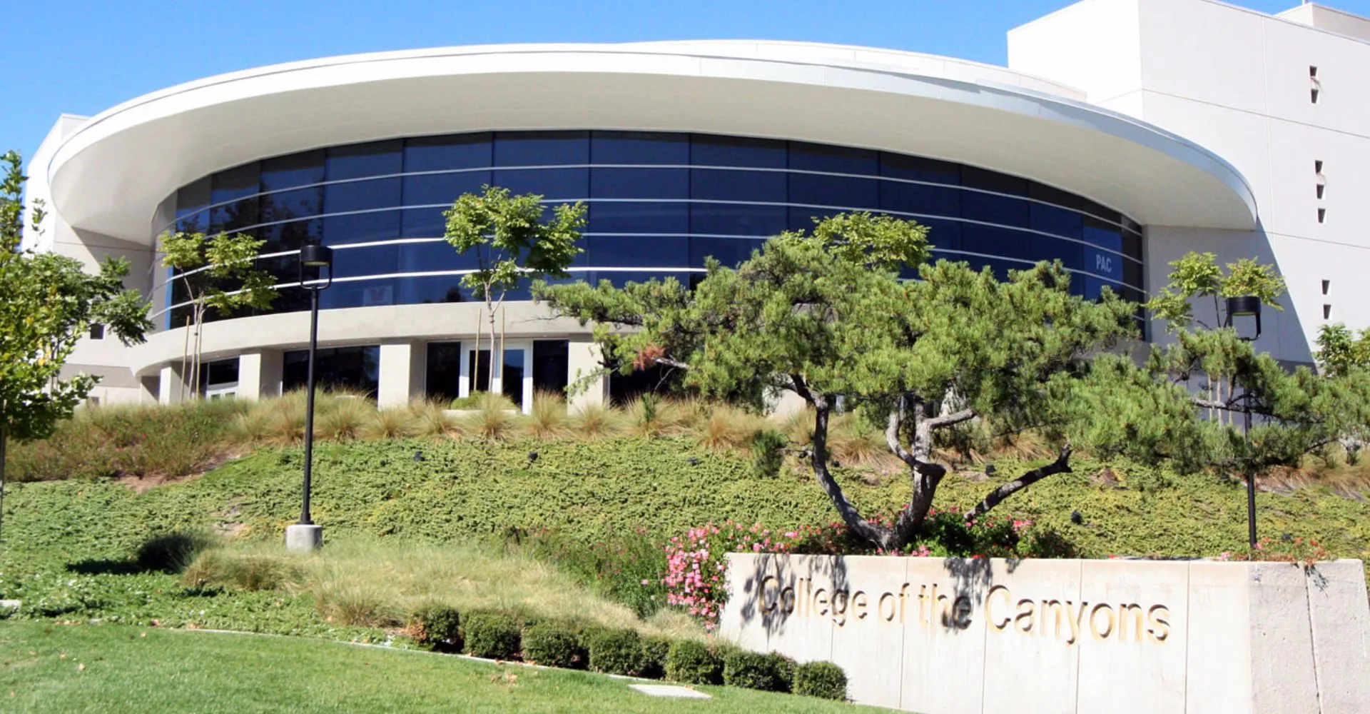 L'edificio moderno del College of the Canyons con una facciata curva in vetro dietro una collina verde con l'insegna.