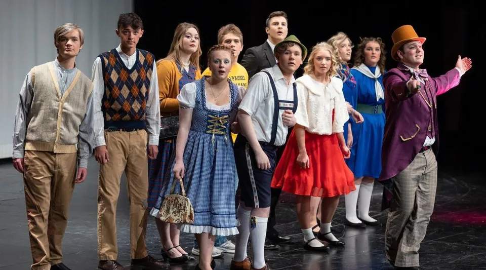 Un gruppo di studenti e studentesse sta in piedi con abiti colorati su un palco della South Christian High School.