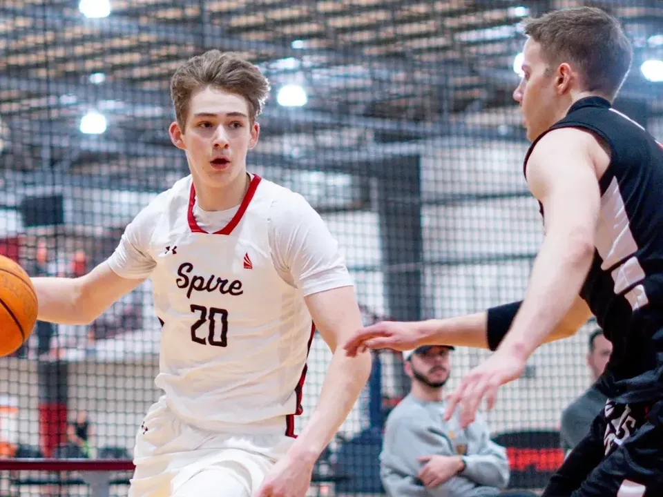 Due studenti della SPIRE Academy giocano a basket su un campo all'aperto con il panorama della città sullo sfondo.